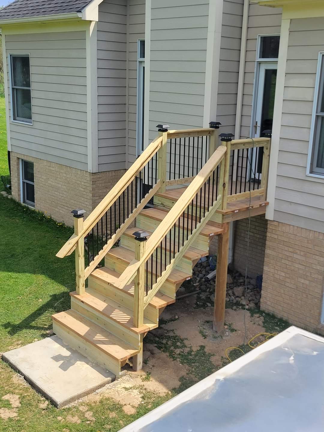 A wooden deck with stairs and metal post caps leading to a backyard.