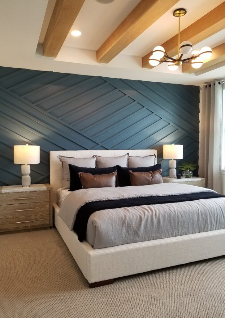 Turquoise geometric wood panel accent wall with white bedframe, wood end tables, white lamps, and gray bedding with brown, black, and gray pillows.